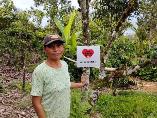 a woman stands with a sign in Indonesian